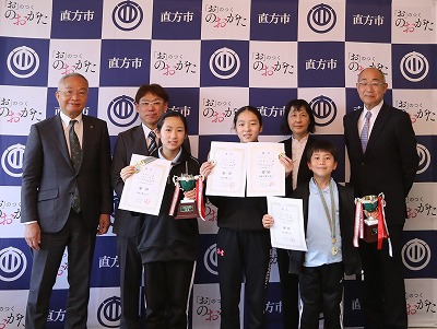 優勝報告に来た小学生が賞状やトロフィーを持って、市長、教育長たちが写っている写真